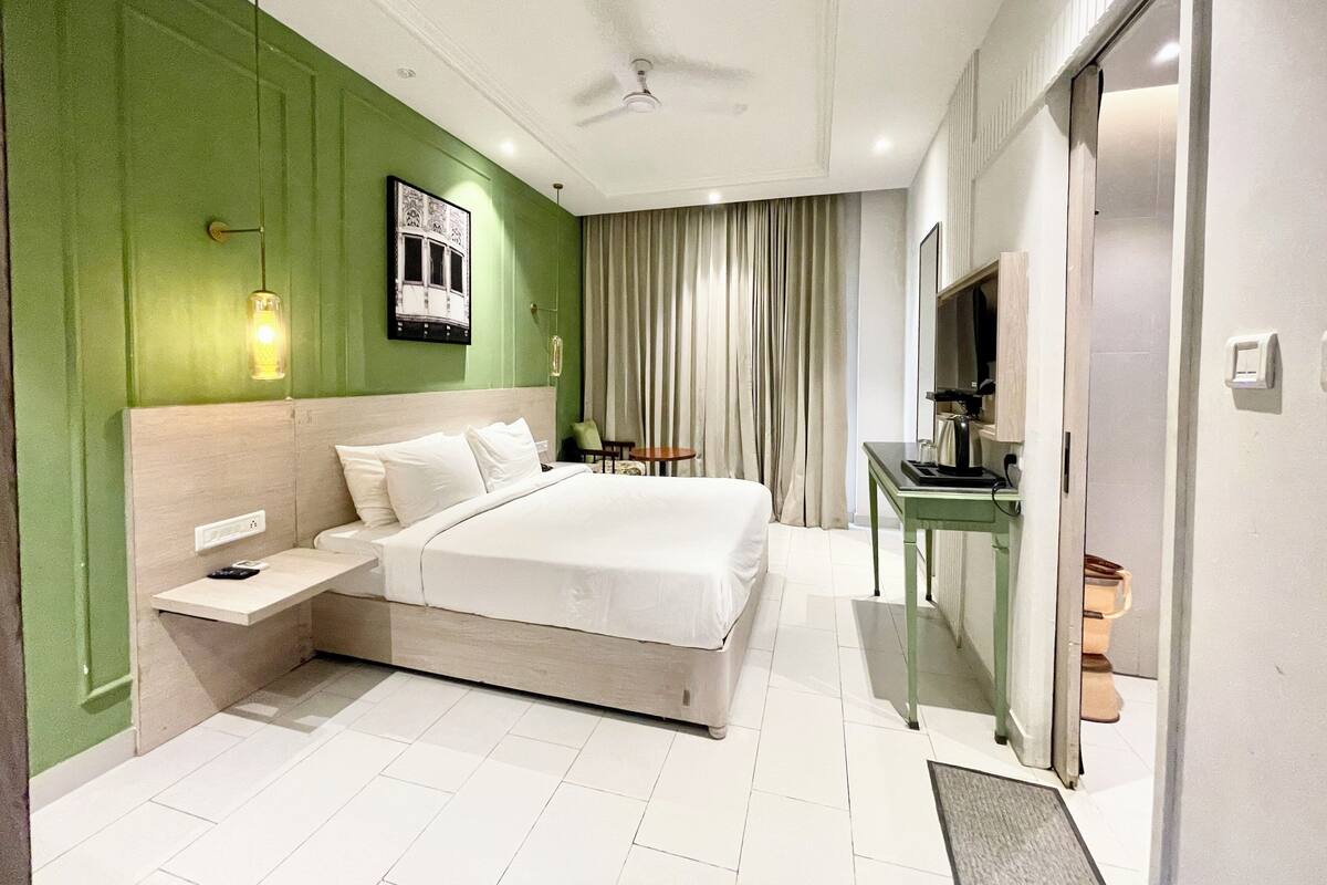 A modern hotel room with a large bed, a desk, a television, and a ceiling fan.