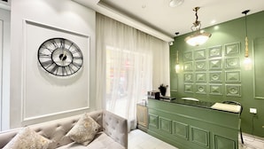 Een moderne woonkamer met een bank, een wandklok en een groene accentmuur met decoratieve panelen.