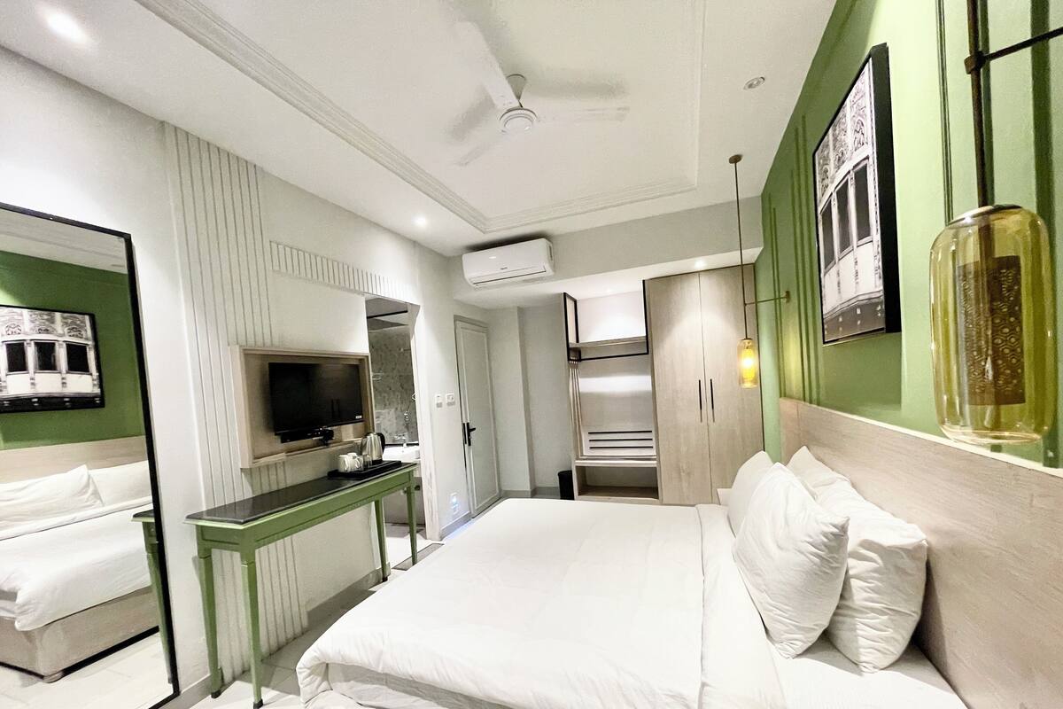 A modern hotel room with a bed, a desk, a television, and a mirror.