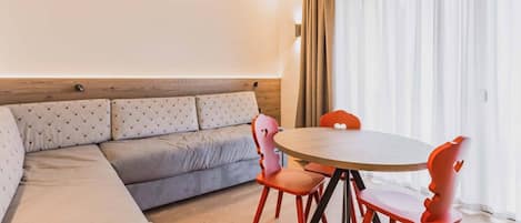 A modern living room with a grey sofa, a round wooden table, and red chairs.