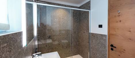 Une salle de bain moderne avec une douche à parois de verre, un lavabo blanc et une porte en bois.