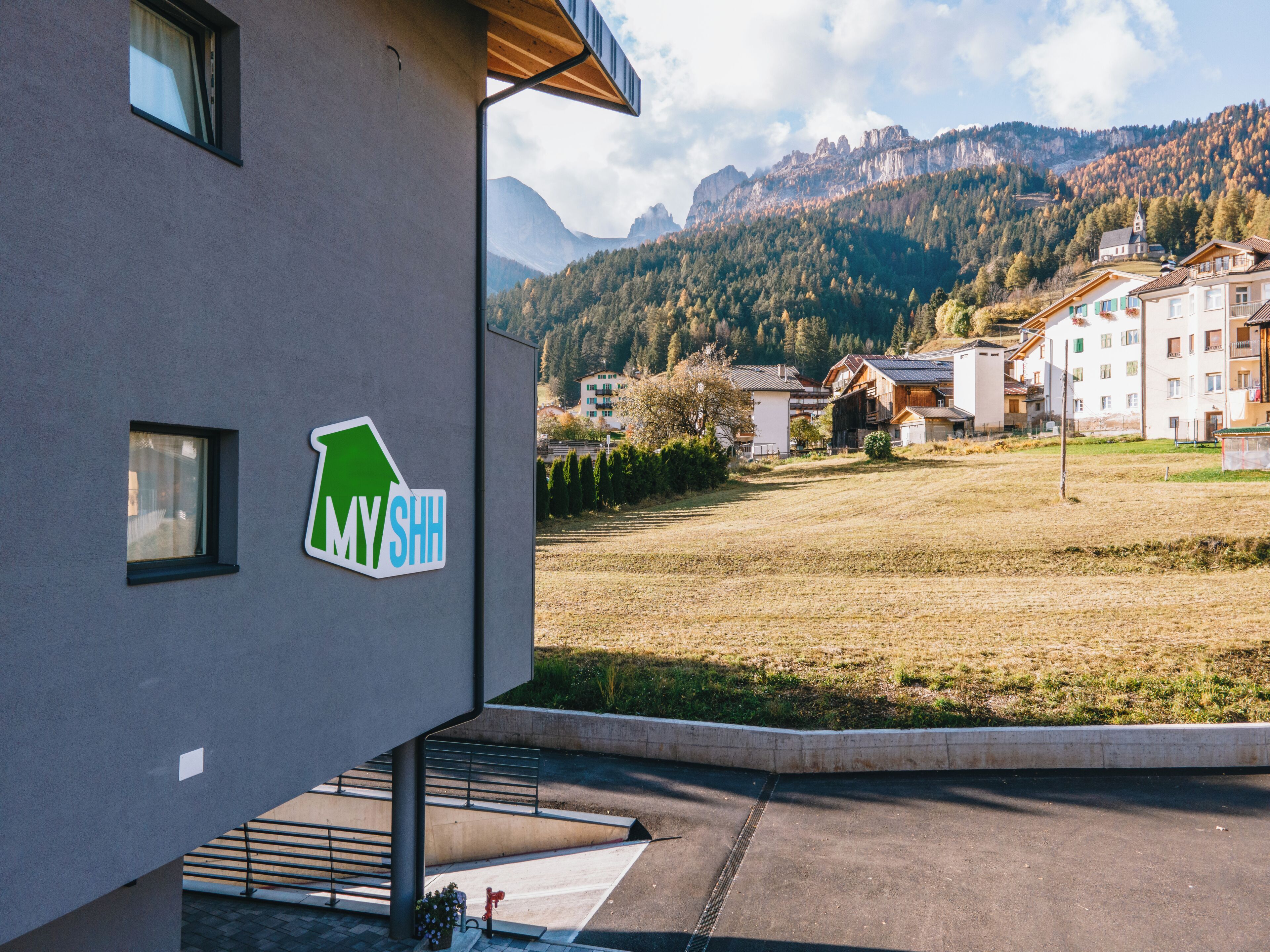 A modern building with a sign reading "MYSHH" and a view of a mountainous landscape with residential buildings.
