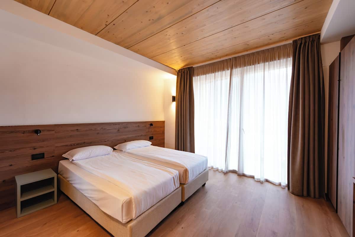 Una cama doble con cabecera de madera, una mesita de noche y una ventana con cortinas.