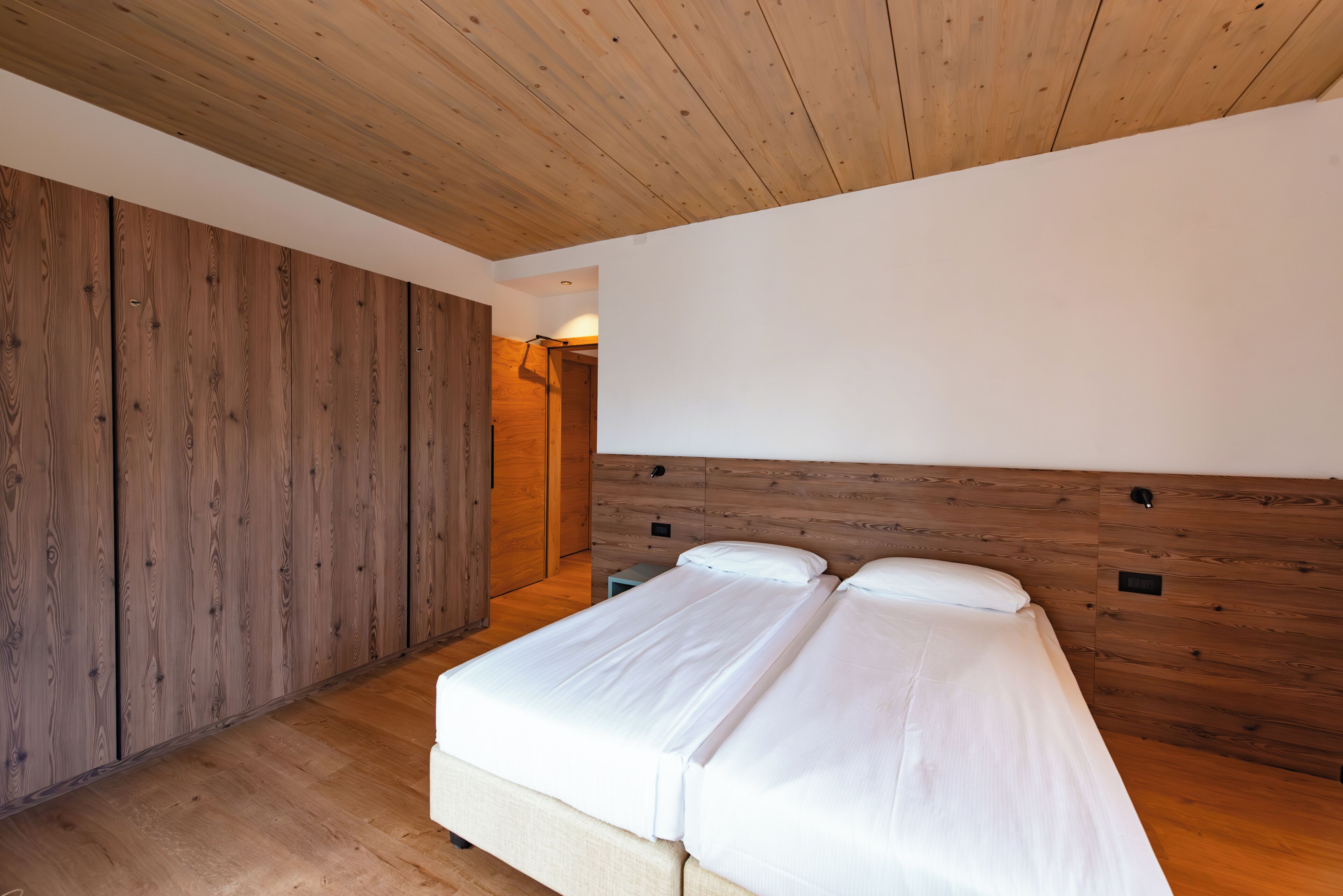 Une chambre avec un plafond en bois, une grande armoire et un lit recouvert de linge de lit blanc.