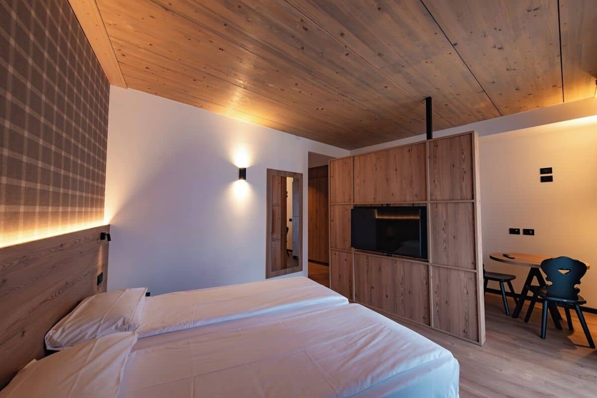 Un dormitorio moderno con techo de madera, una cama con ropa blanca, un televisor y un pequeño comedor con sillas.