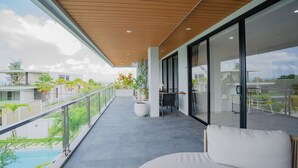 A modern balcony with a wooden ceiling, a seating area with a white cushion, and a view of a swimming pool and greenery. - Gandum Uluwatu Luxury Boutique Stay - Gandum Villa Complex (Pecatu)