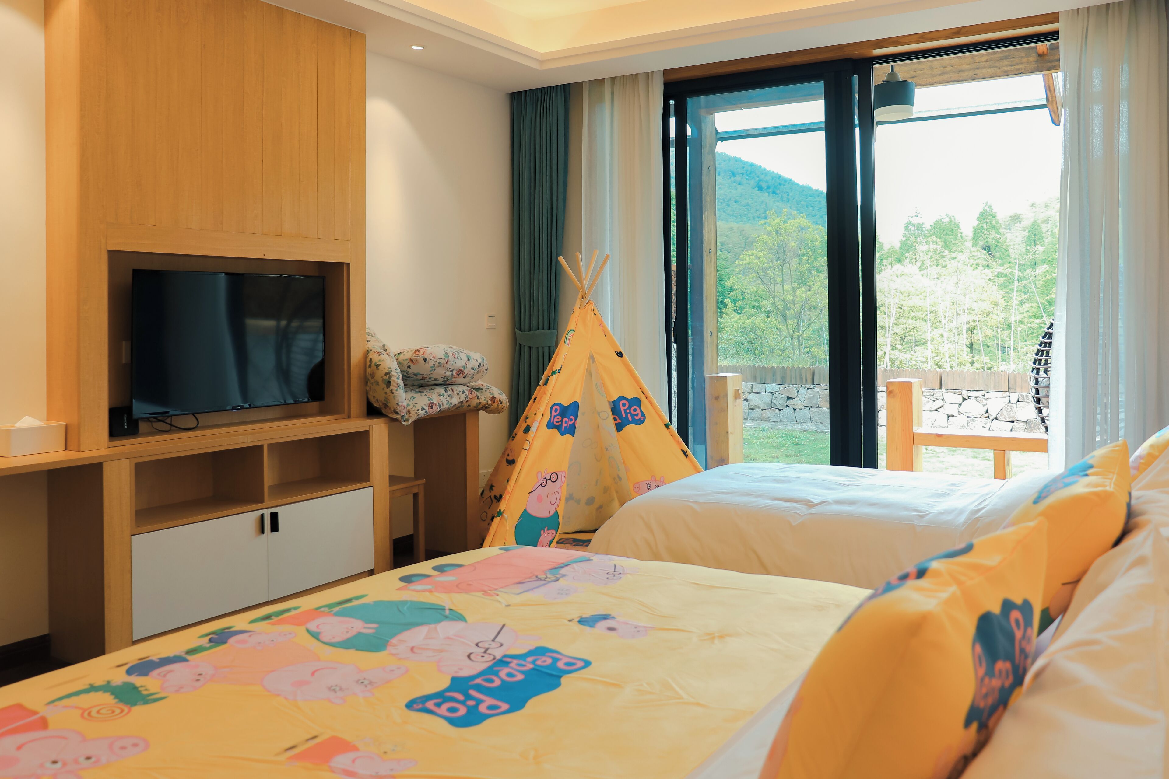 Une chambre d’hôtel avec deux lits, une télévision, une armoire en bois, une fenêtre donnant sur un paysage verdoyant et un tipi.