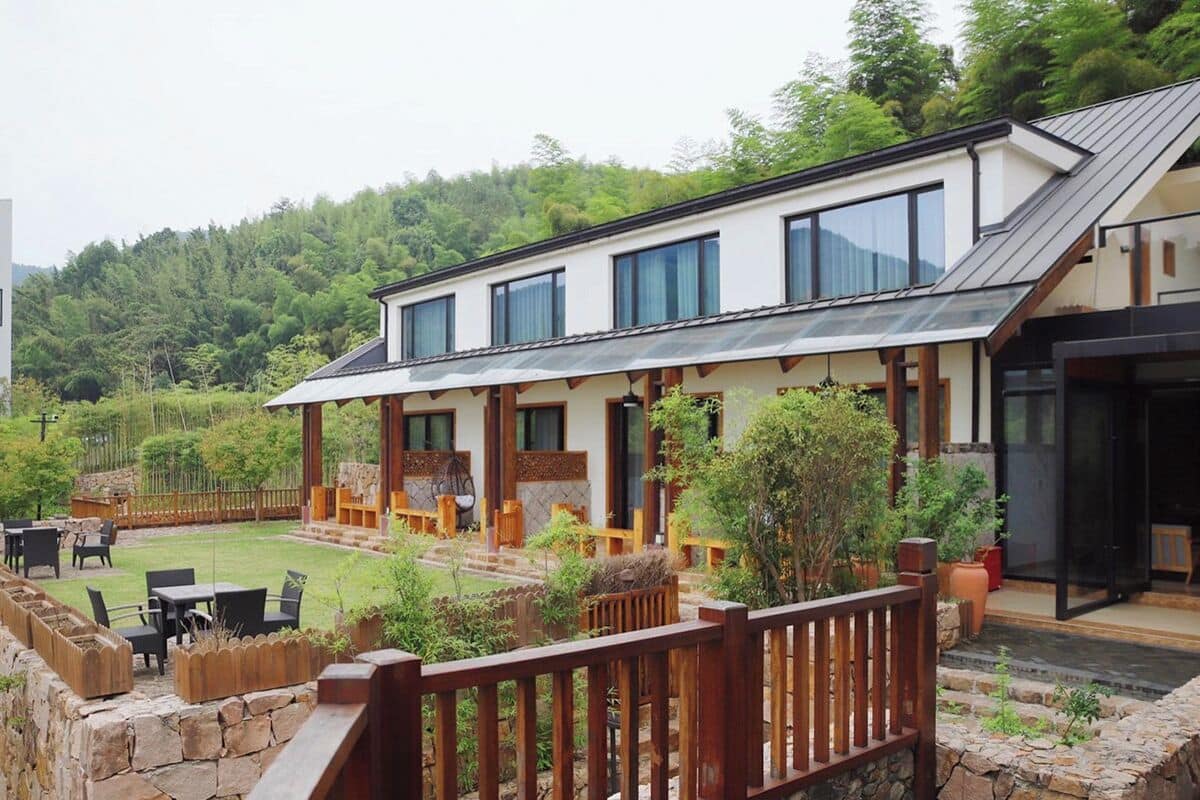 Une maison moderne à deux étages, dotée d’un patio couvert, de murs en pierre et d’une terrasse en bois.
