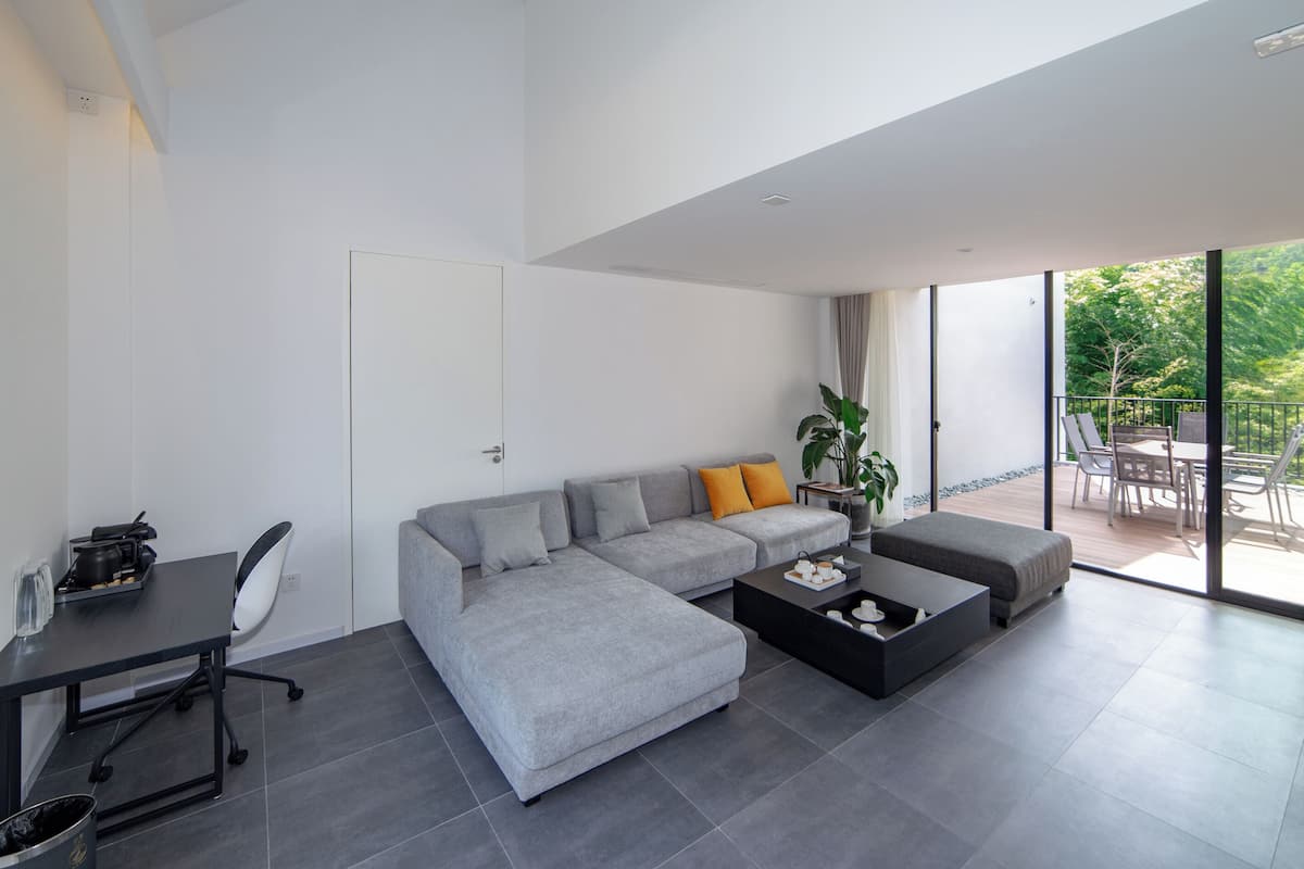 Un salon moderne avec un canapé d’angle gris, une table basse noire et un coin repas comprenant une table et des chaises.