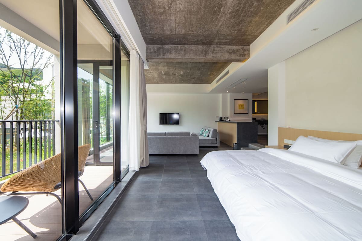 Une chambre d’hôtel moderne dotée d’un grand lit, d’un canapé, d’une télévision et d’un balcon aménagé avec des meubles en osier.