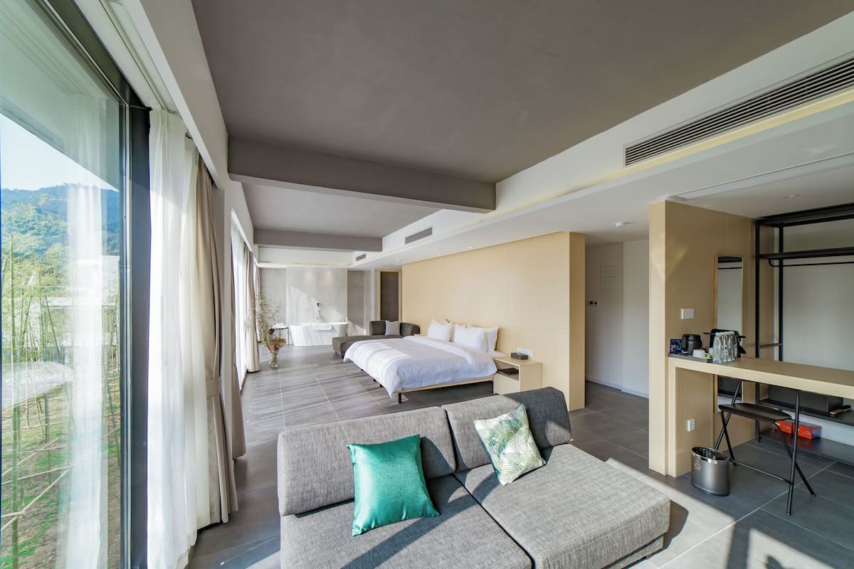 Une chambre d’hôtel moderne, dotée d’un grand lit, d’un canapé, d’un bureau et offrant une vue sur l’extérieur.