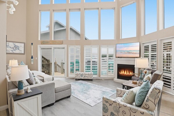 A spacious living room with a fireplace, large windows, and a view of the outside.