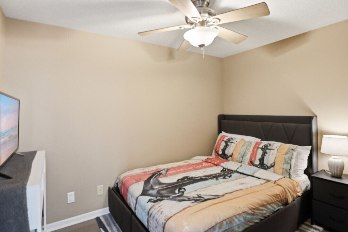 A bedroom with a bed, a ceiling fan, a TV, and a nightstand.