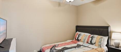 A bedroom with a bed, a ceiling fan, a TV, and a nightstand.