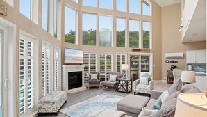 Un salón espacioso con chimenea, asientos cómodos, ventanas grandes y vistas al exterior.