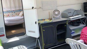 A compact RV interior with a bed, kitchenette, and a small table with a fan.