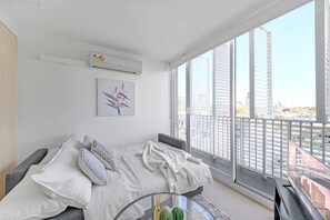 Une chambre moderne avec un lit, des oreillers, une table en verre et une vue sur la ville.