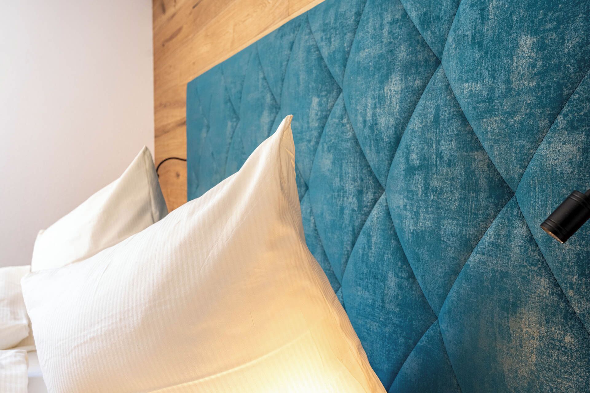 A bed with white pillows and a blue quilted headboard.
