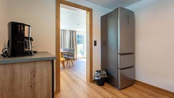 A compact kitchen with a coffee machine, a stainless steel refrigerator, and a wooden floor.