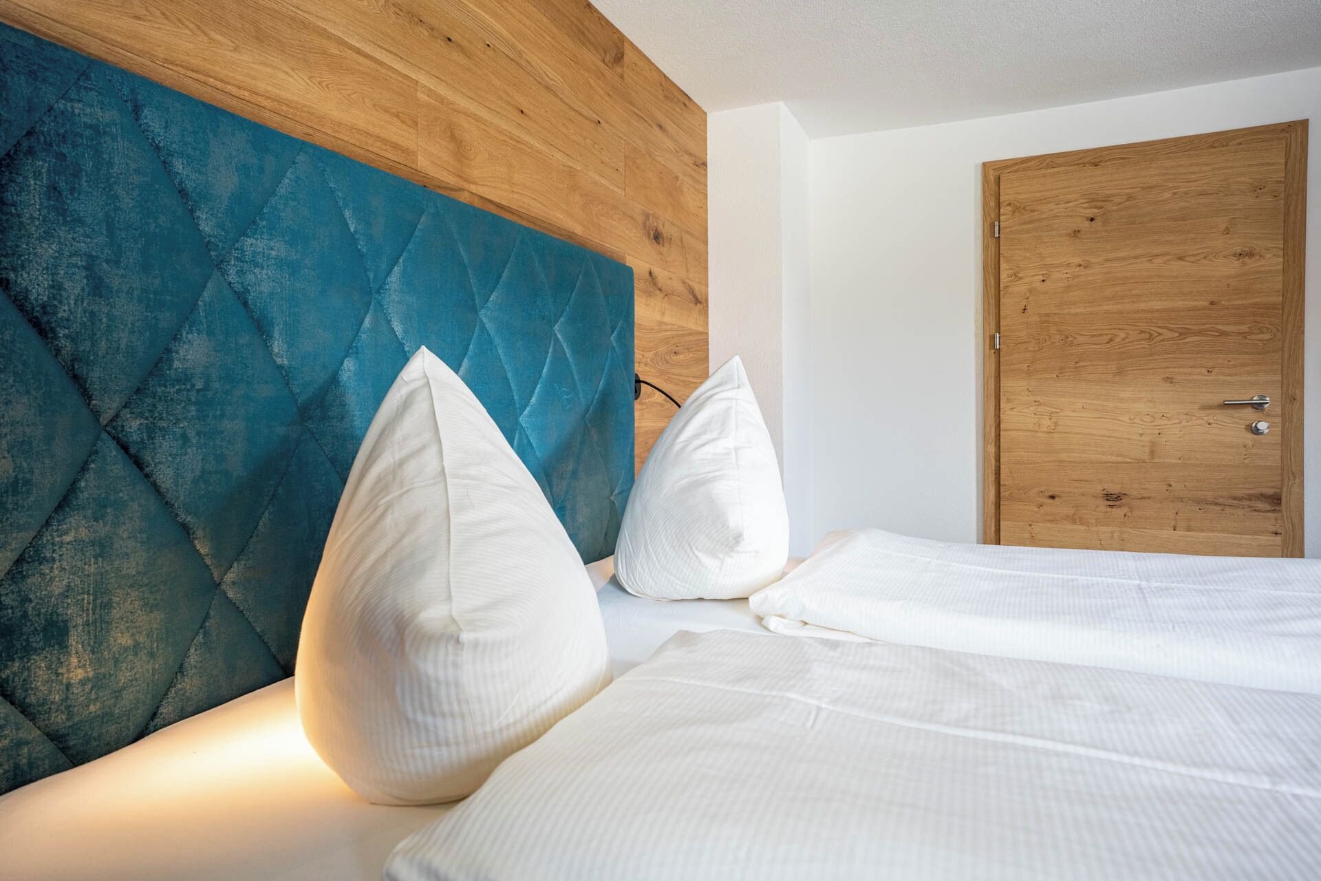 Una habitación de hotel con cabecera y puerta de madera, y una cama con ropa y almohadas blancas.