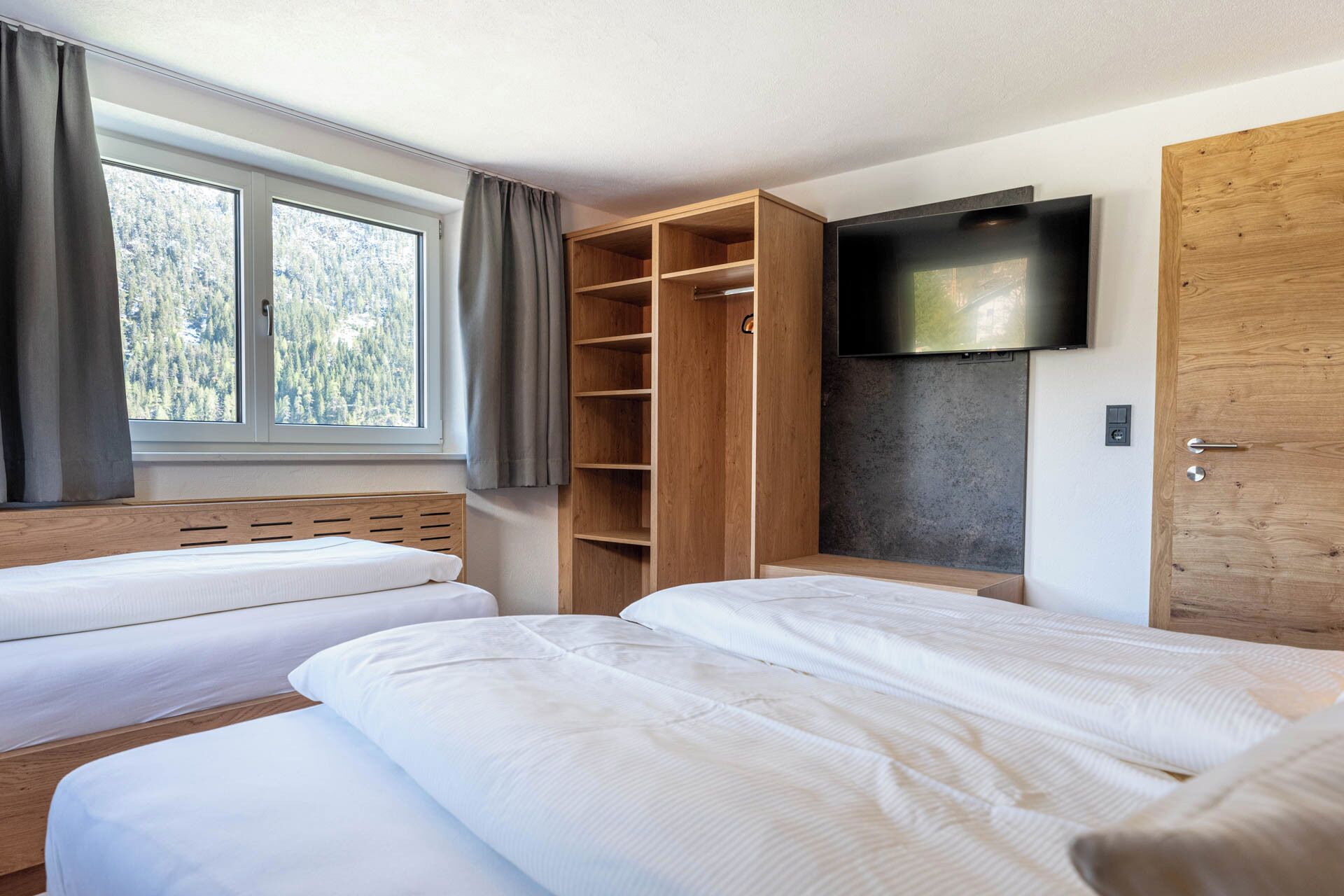 Un dormitorio con dos camas, un armario, un televisor y una ventana con cortinas.
