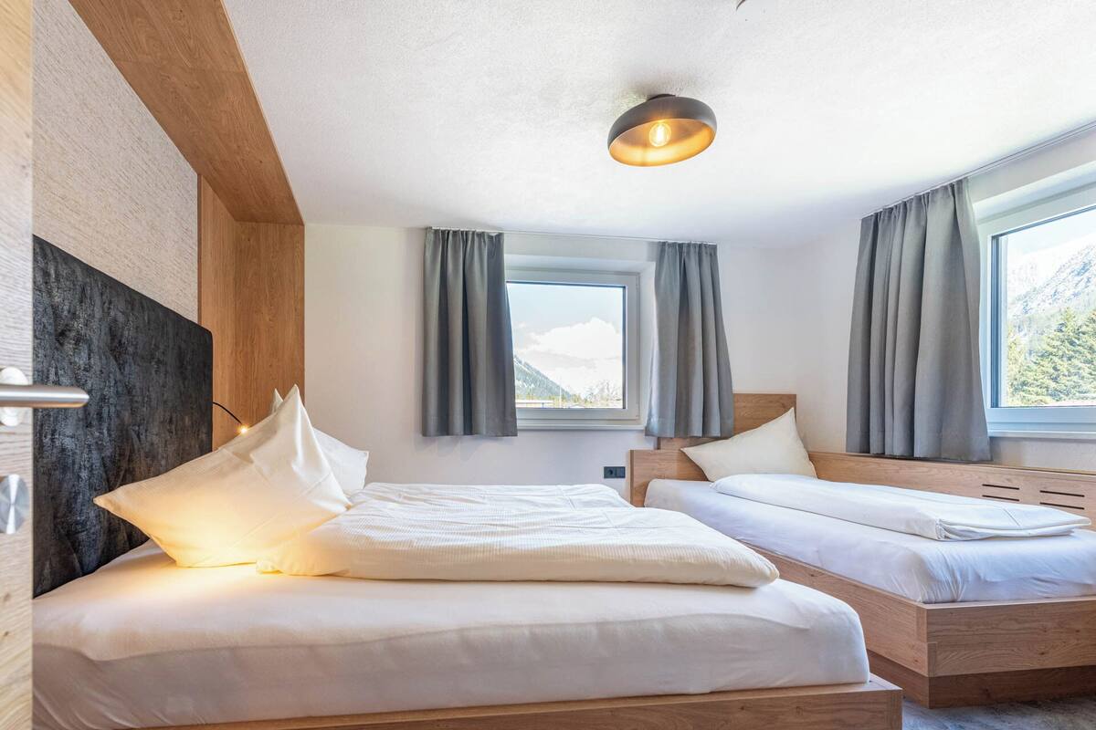 A hotel room with two beds, a wooden headboard, a large window with curtains, and a ceiling light.