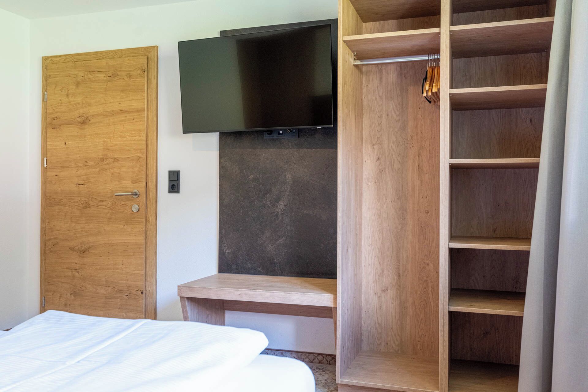 Quarto com armário de madeira, uma cama e televisão na parede.