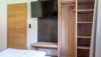 Quarto com armário de madeira, uma cama e televisão na parede.
