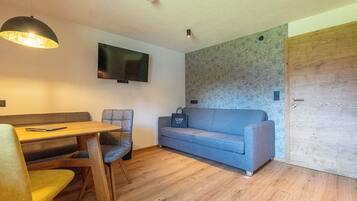 A compact living space with a wooden dining table, two chairs, a sofa, and a television mounted on the wall.