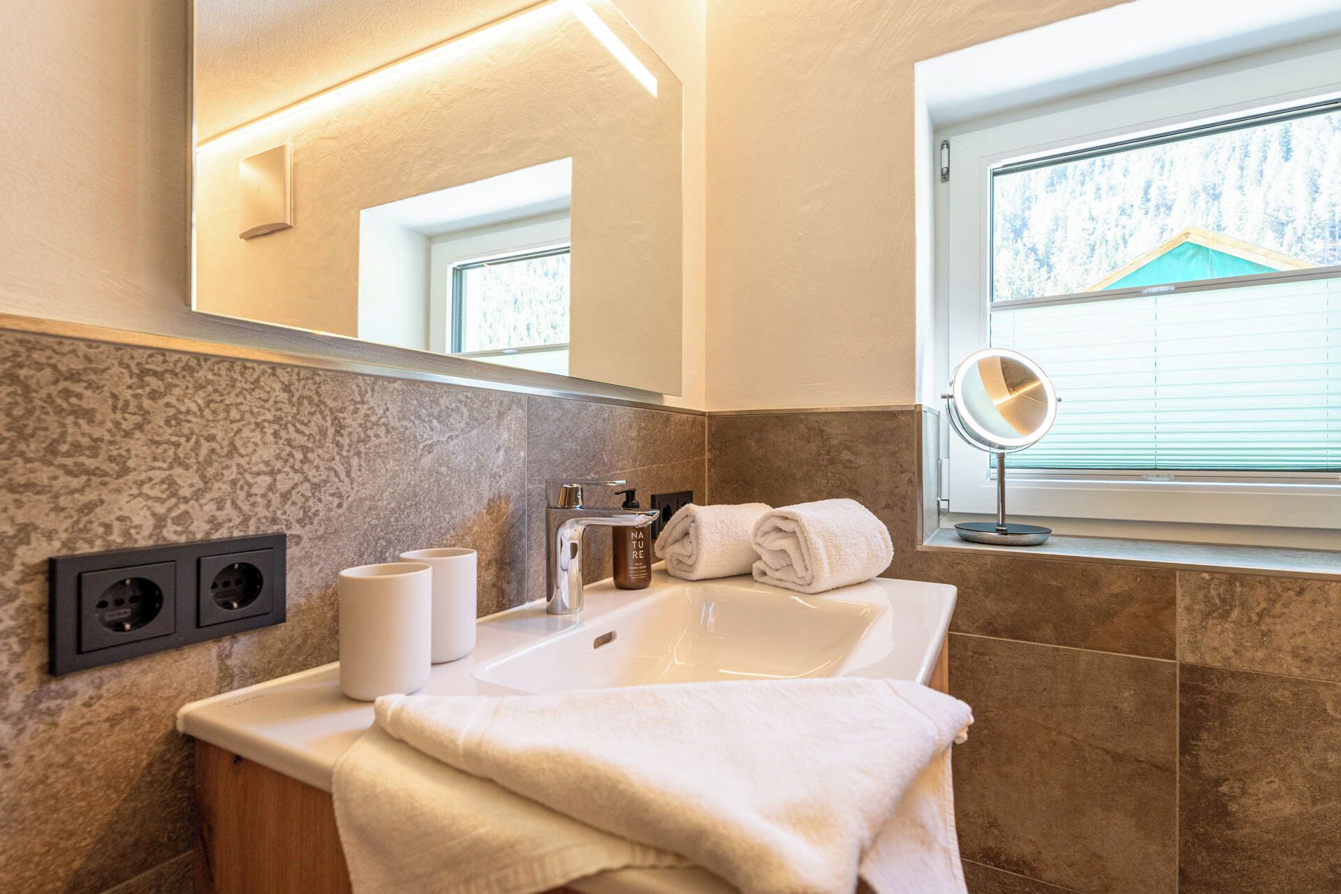 A bathroom with a sink, mirror, and two outlets on the wall.