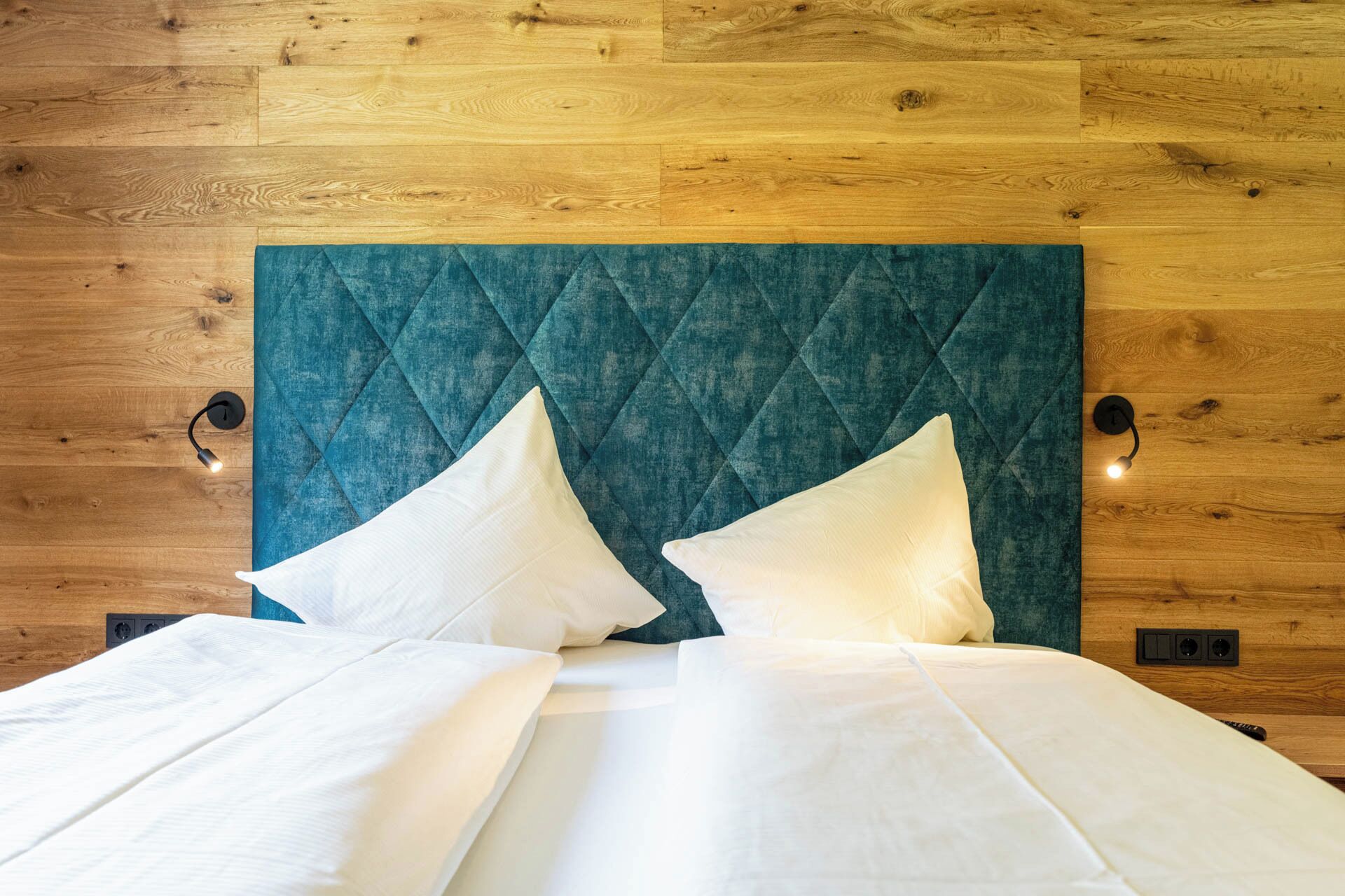 A bed with a quilted teal headboard, two white pillows, and a white bedspread.