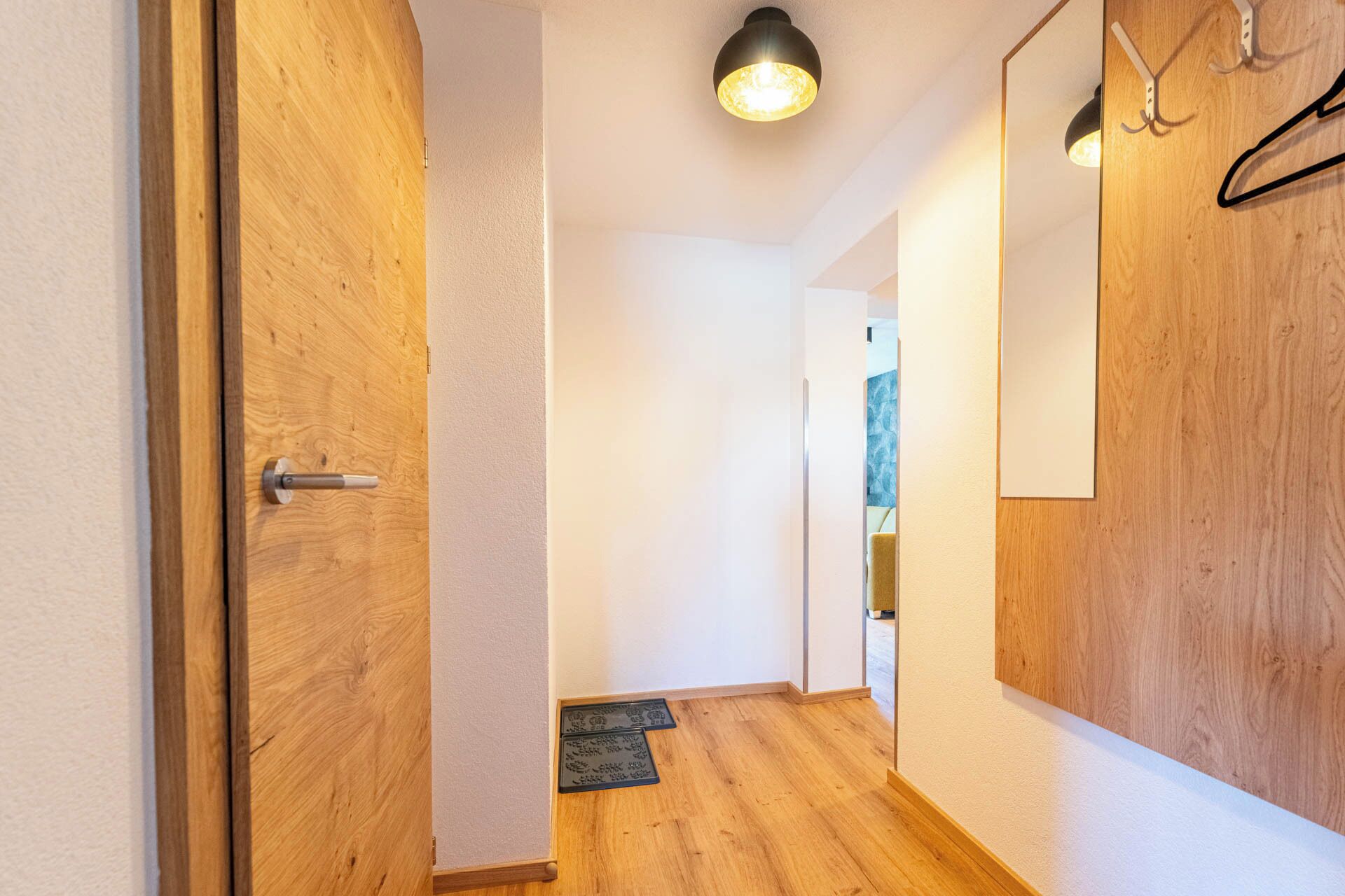 Un pasillo con puertas de madera, un aplique, un espejo y un colgador de puerta.
