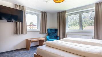Una habitación de hotel con una cama, una silla, un escritorio y un televisor montado en la pared.