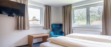 Una habitación de hotel con una cama, una silla, un escritorio y un televisor montado en la pared.
