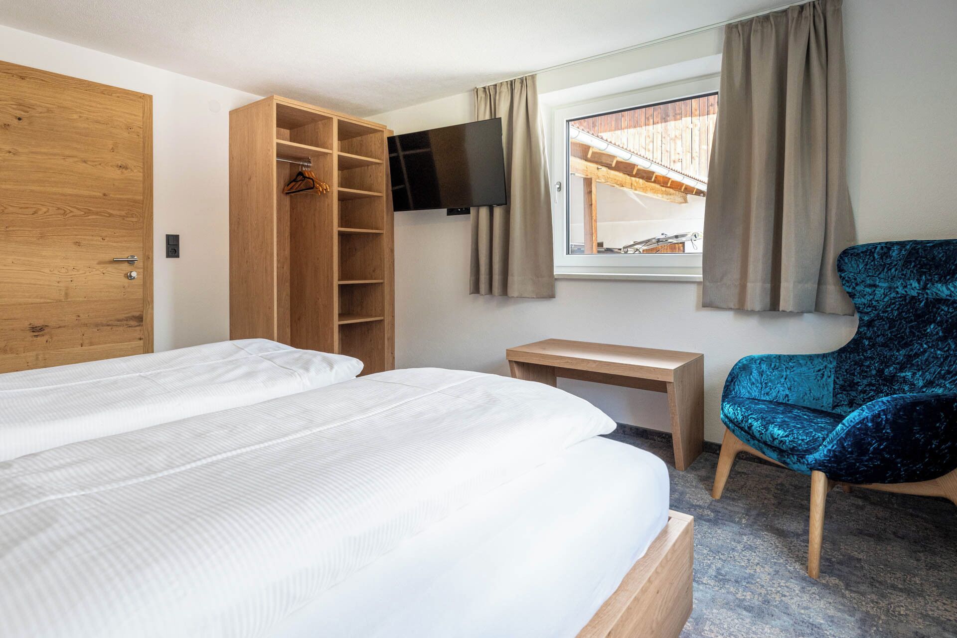 Habitación de hotel con cama, armario de madera, escritorio, silla y televisor montado en la pared.