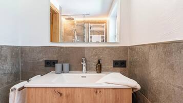A modern bathroom with a wooden vanity, a large mirror, and a shower area visible in the reflection.