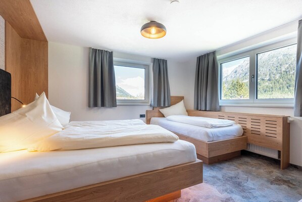 A modern bedroom with two beds, large windows, and a view of mountains.