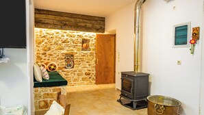 Una habitación acogedora con pared de piedra, puerta de madera, estufa y una olla en el suelo.