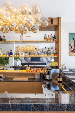 Eine Bar mit modernem Design, darunter eine besondere Leuchte, Regale mit verschiedenen Spirituosen und eine Marmor Arbeitsplatte.