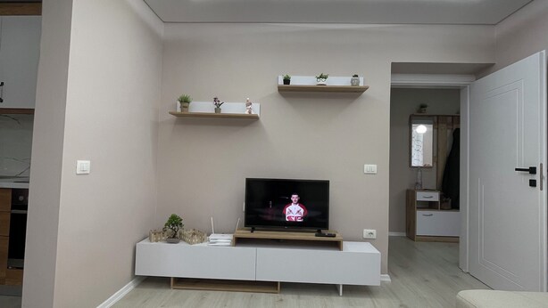 A modern living room with a flat-screen TV on a wooden stand, a white coffee table, and built-in shelves with decorative items.