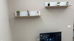 A modern living room with a flat-screen TV on a wooden stand, white entertainment unit, and two shelves with decorative items.