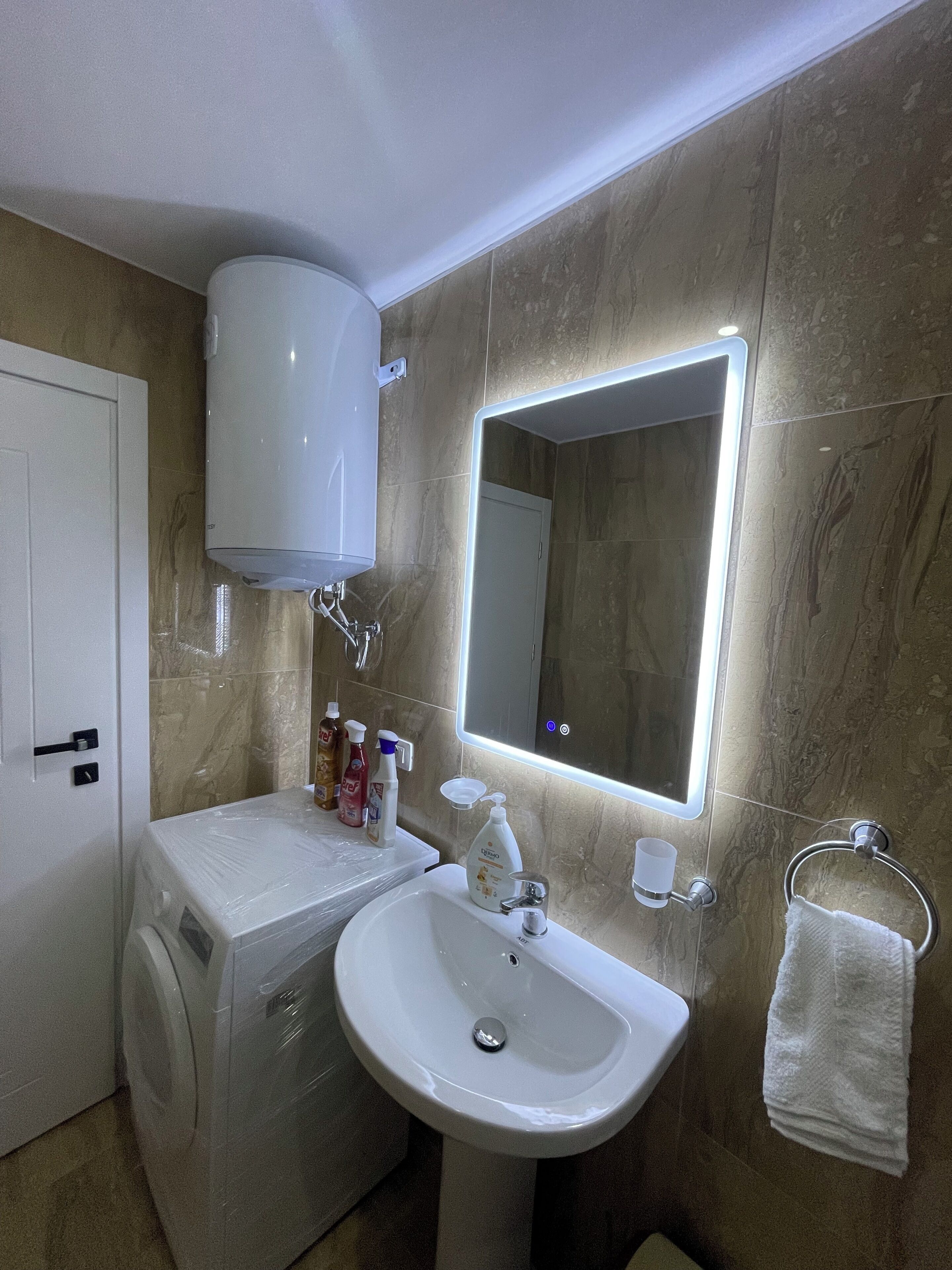 Une salle de bain avec un lavabo blanc, un miroir, un porte-serviettes et un lave-linge.