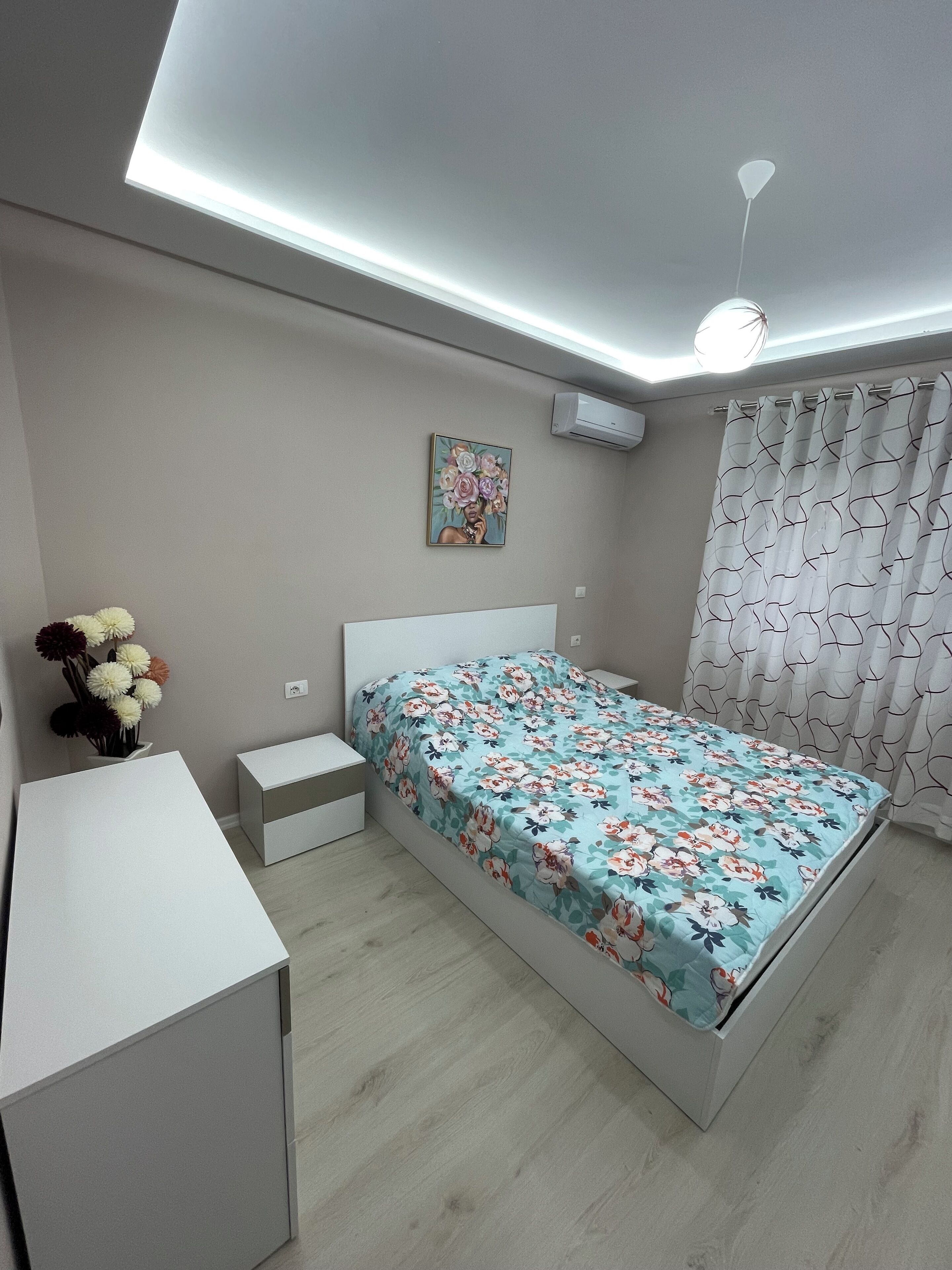 A modern bedroom with a bed, bedside tables, a desk, and a ceiling light.