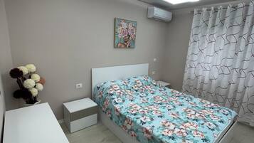 A modern bedroom with a bed, bedside tables, a desk, and a ceiling light.