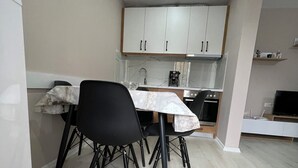 A compact kitchen with white cabinets, a marble countertop, and a black chair.