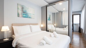 A hotel room with a bed, a nightstand, a lamp, a large mirror, and a painting on the wall. - Athens Horizon Acropolis Views Apartment (Athens)