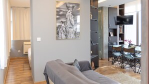 A modern living room with a grey sofa, a flat-screen TV mounted on the wall, and a dining area with a table and chairs. - Athens Horizon Acropolis Views Apartment (Athens)