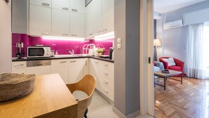 Una cocina moderna con armarios blancos, salpicadero rosa y un comedor con mesa y silla de madera.