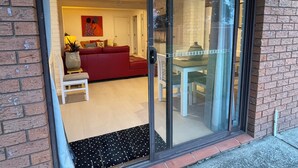 A modern living room with a red sofa, a white table, and a glass door leading to a patio area. - Beachfront Bliss on the Jervis Bay (Vincentia)