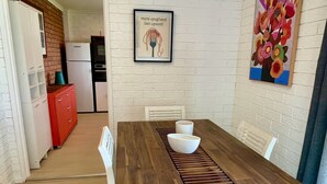 A dining area with a wooden table, white chairs, and a kitchen in the background. - Beachfront Bliss on the Jervis Bay (Vincentia)